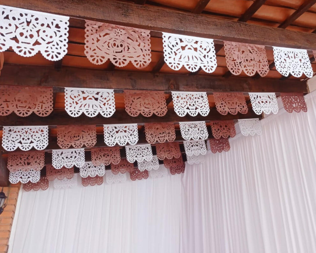 Decorative lace brown and white tissue paper garlands hanging from a wooden beam with a white curtain in the background.