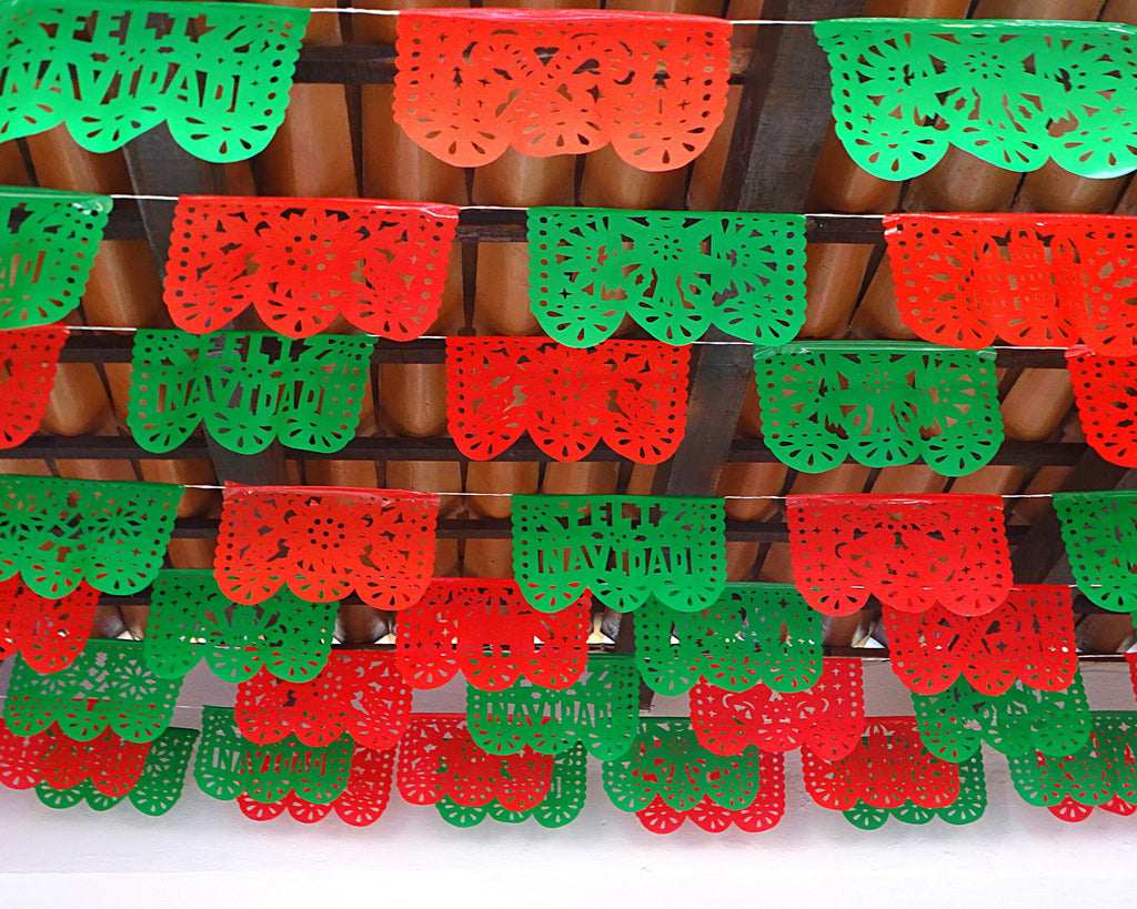 Red and green paper garlands with Feliz Navidad cut outs hanging against a wooden background