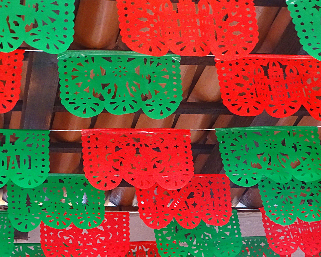 Red and green papel picado hanging on a wooden surface