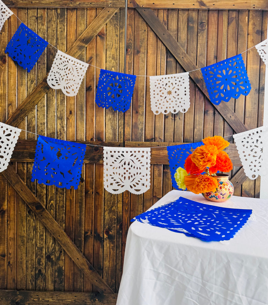 Decorative papel picado with blue, white, and orange flowers on a wooden backdrop