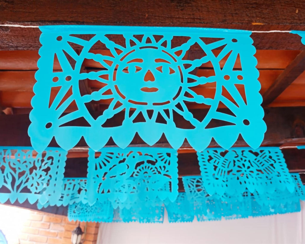 Turquoise papel picado with sun design hanging against a wooden wall.