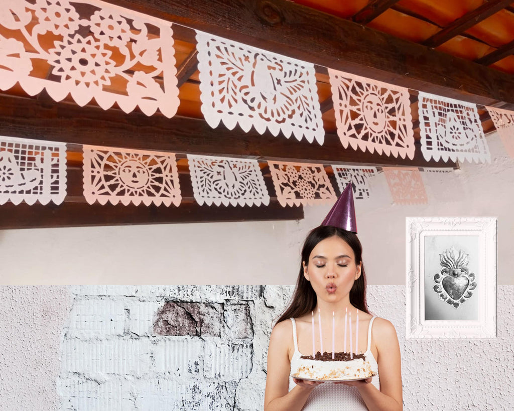 Woman blowing out candles on a birthday cake with papel picado in the background