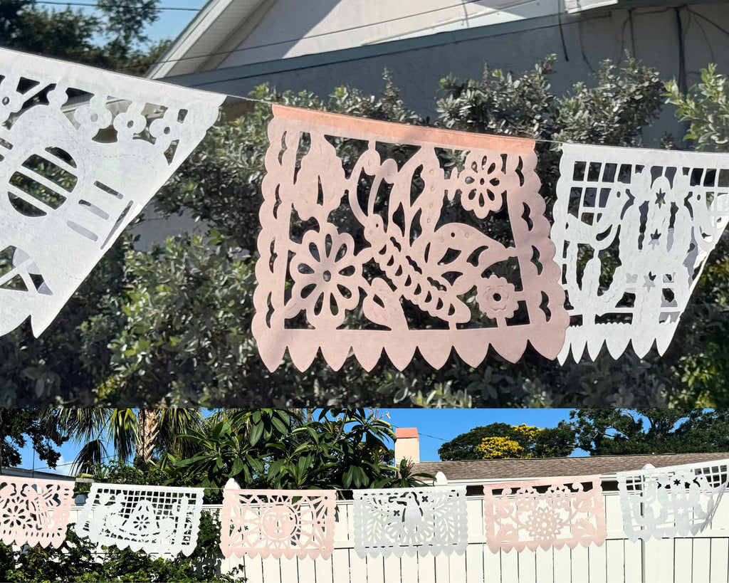 Decorative paper banners in pink and white hanging outdoors with trees and a house in the background.