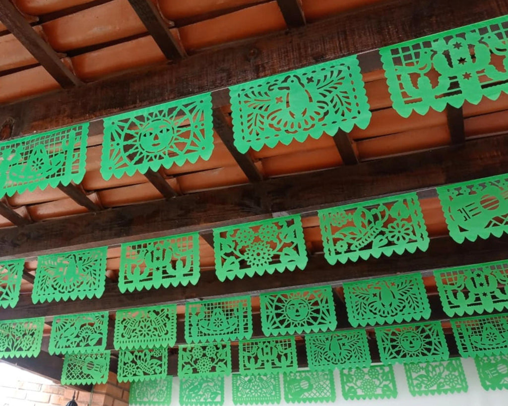 Green paper cutout PAPEL Picado decorations hanging from a wooden ceiling
