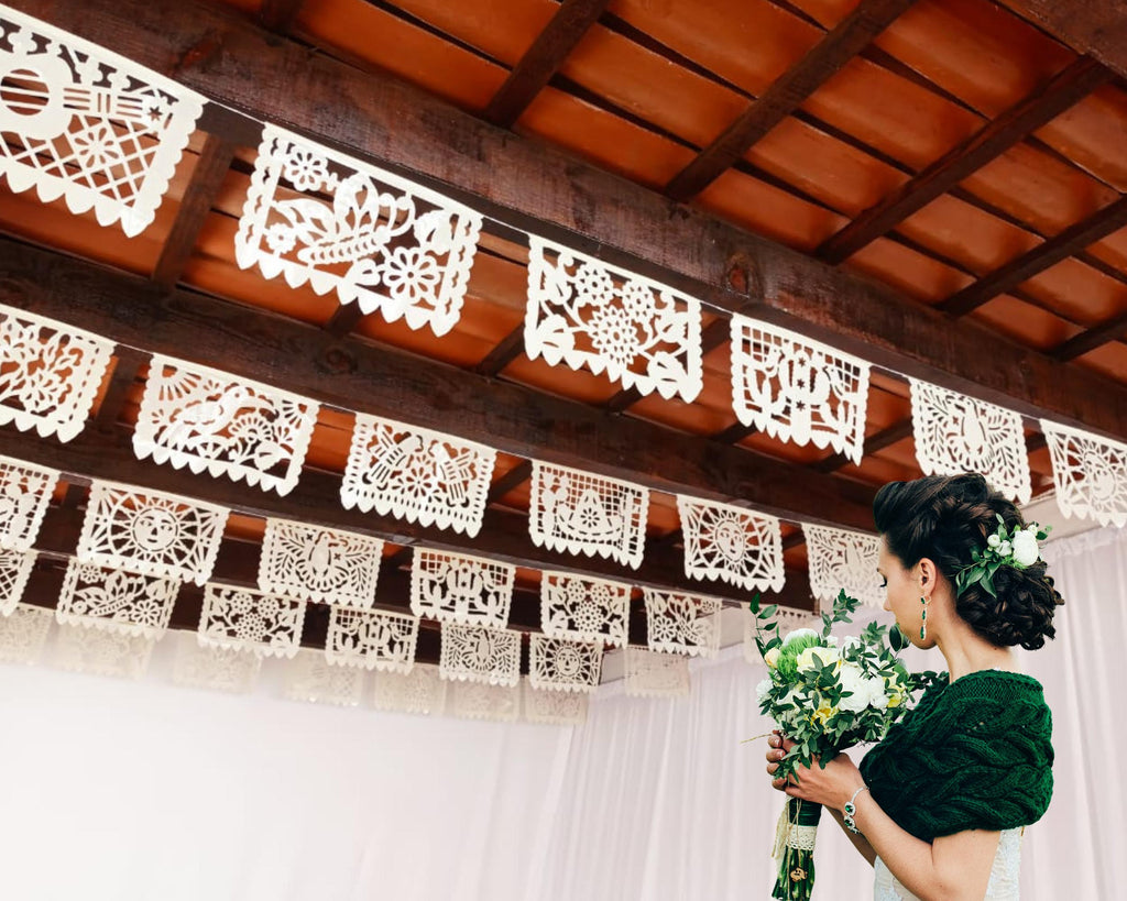 Woman holding a bouquet under decorative papel picado against a wooden ceiling.
