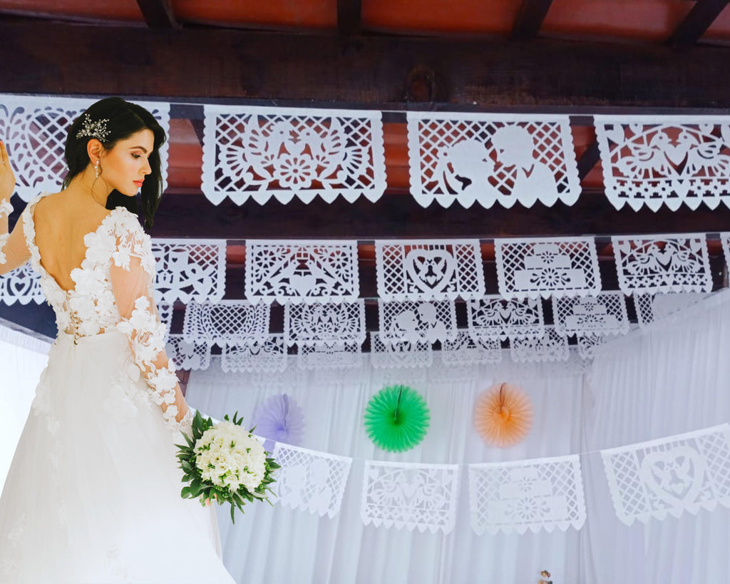 Woman in a white wedding dress standing in front of decorative wedding papel picado and colorful paper decorations.