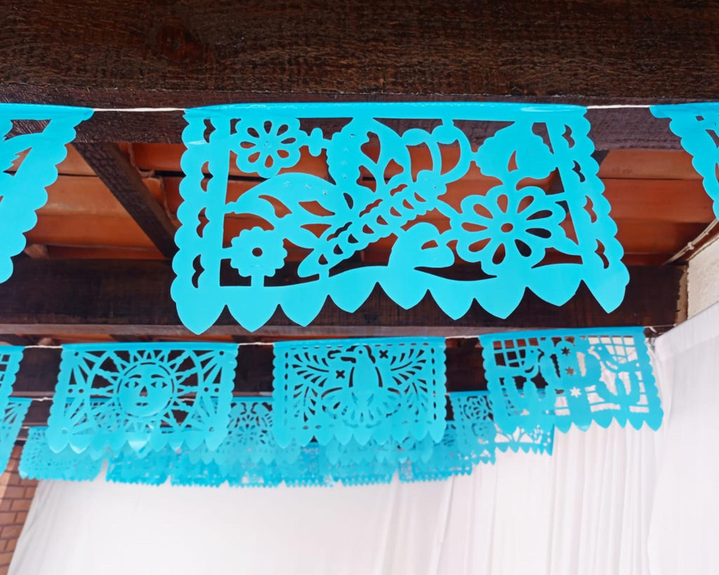 blue papel picado banner on a wooden surface with a white curtain in the background.